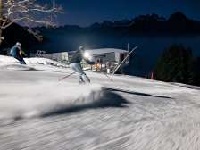 Deux skieurs regardent la vallée du Rhin éclairée lors d'une séance de ski nocturne au Pizol.