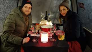 Un couple déguste une fondue au fromage dans une gondole, assis à une table bien garnie.