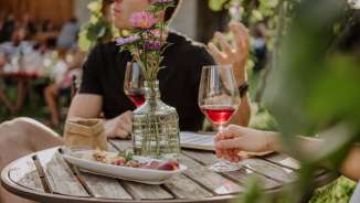 Wii-kend Maienfeld Couple assis à une table en bois avec une décoration estivale, des snacks et un verre de vin.