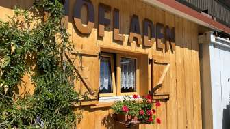 Une cabane en bois avec des fleurs et l'inscription "Hofladen" (magasin à la ferme)