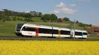 Un train de 3 wagons traverse un paysage printanier en Suisse