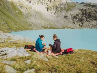 Couple assis sur une couverture de pique-nique devant un lac de montagne bleu glacial