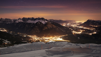 Vue sur le Sarganserland hivernal de nuit. Au premier plan, on voit une piste de ski. Dans la vallée, on aperçoit des lumières multicolores.