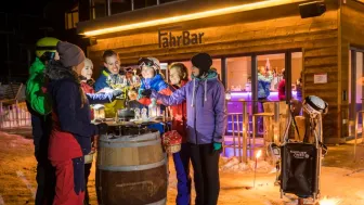 Un groupe d'amateurs de sports d'hiver* se tient devant le FahrBar enneigé et trinque avec des verres de vin.