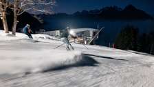 Deux skieurs regardent la vallée du Rhin éclairée lors d'une séance de ski nocturne au Pizol.