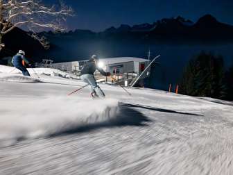 Deux skieurs regardent la vallée du Rhin éclairée lors d'une séance de ski nocturne au Pizol.